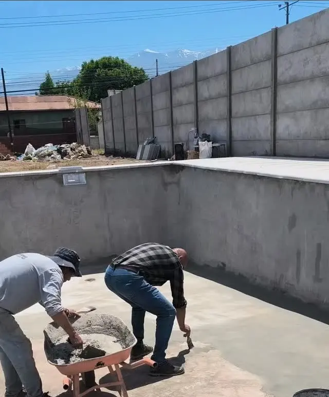 Trabajadores estucando el fondo de una piscina de hormigón con la cordillera al fondo